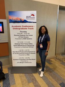 picture of Raenell Shirley at 2019 SHPE standing next to sign with her presentation featured technology consulting